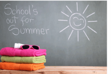 Chalkboard with “School’s out for summer” and a smiling sun drawn in chalk, next to stacked beach towels, pink sunglasses, and sunscreen.
